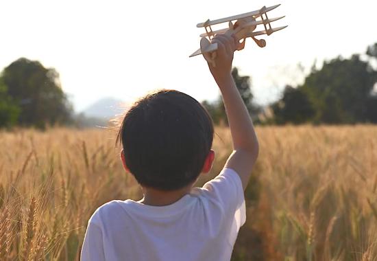 Bambino che gioca con un aeroplanino di legno in mezzo a un campo di grano